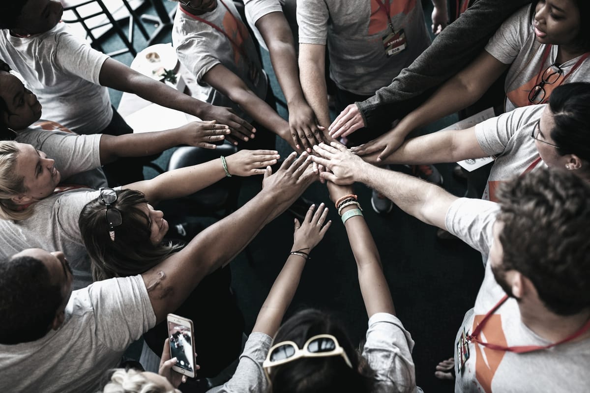 Large team all putting their hands into the middle of a circle
